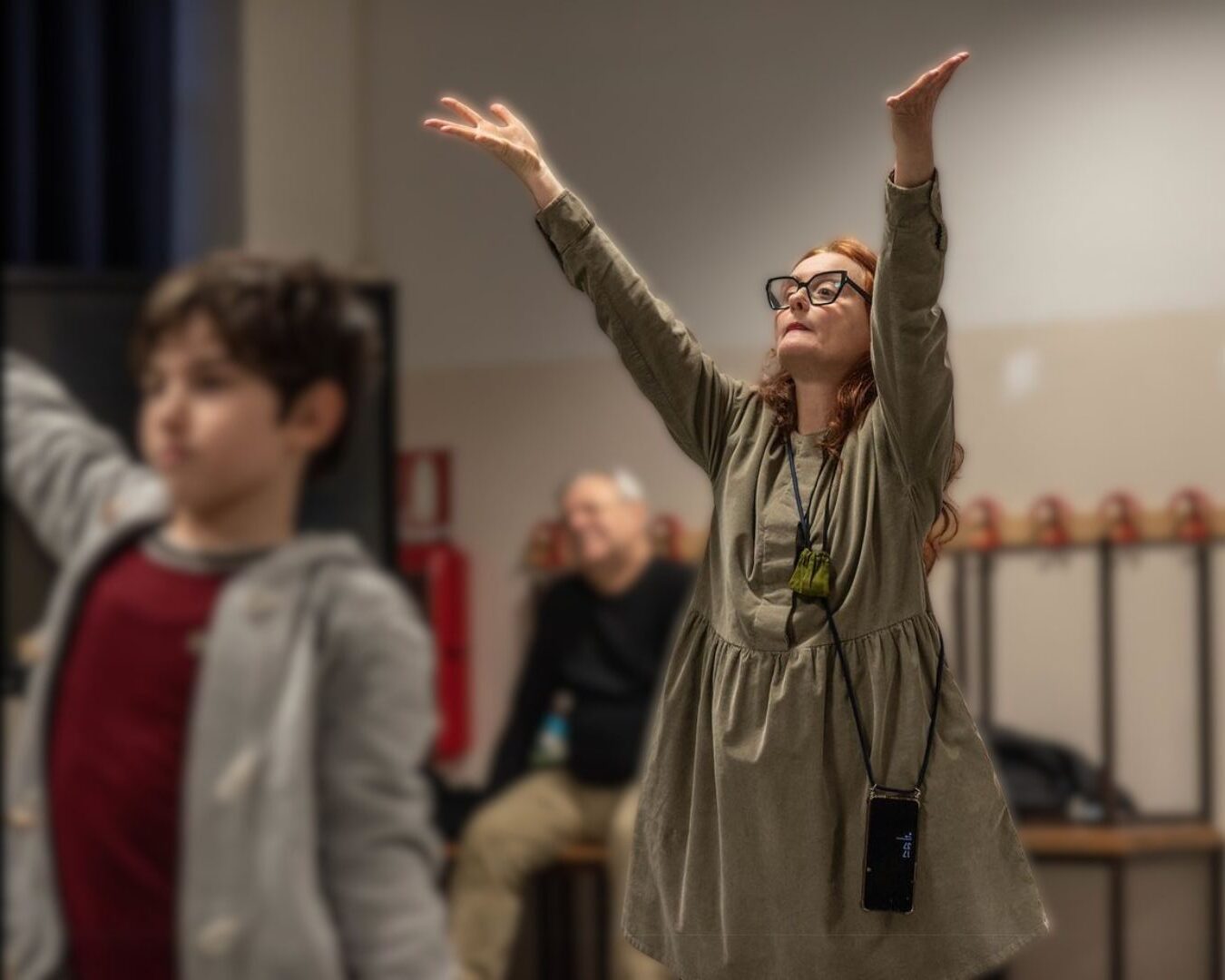Marzia del Teatro del Sorbo Selvatico con le braccia alzate mentre spiega un esercizio pratico di teatro psicomotorio a un gruppo di bambini in classe